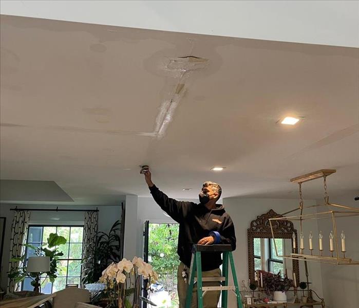 male with black hoodie checking the white ceiling for water damage 