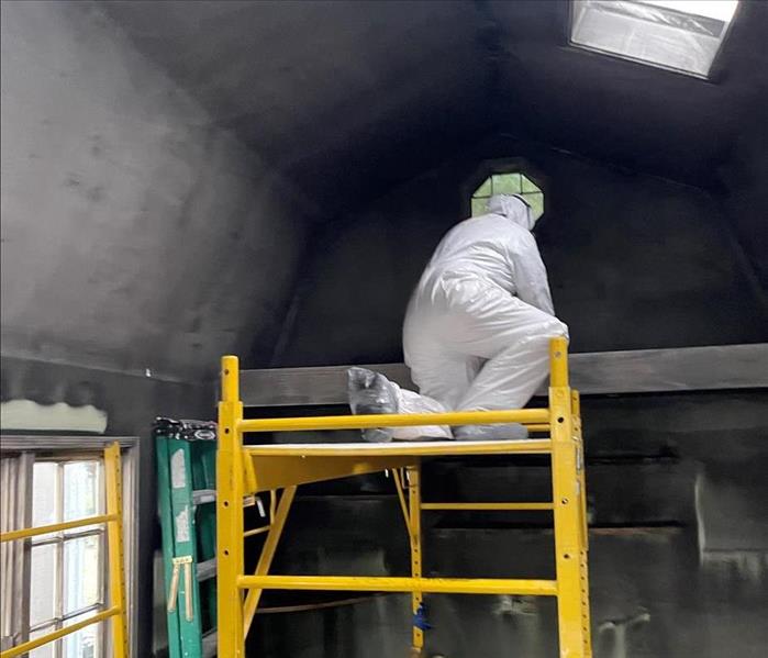 man wearing a white suit cleaning fire damaged walls 